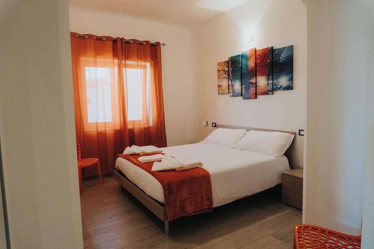 A bedroom with a bed, a chair, a nightstand, and a wall with three paintings.