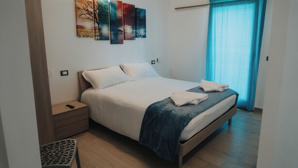 A neatly arranged bedroom with a bed, bedside tables, and a wall-mounted artwork. - Harmony B&B (Leporano)