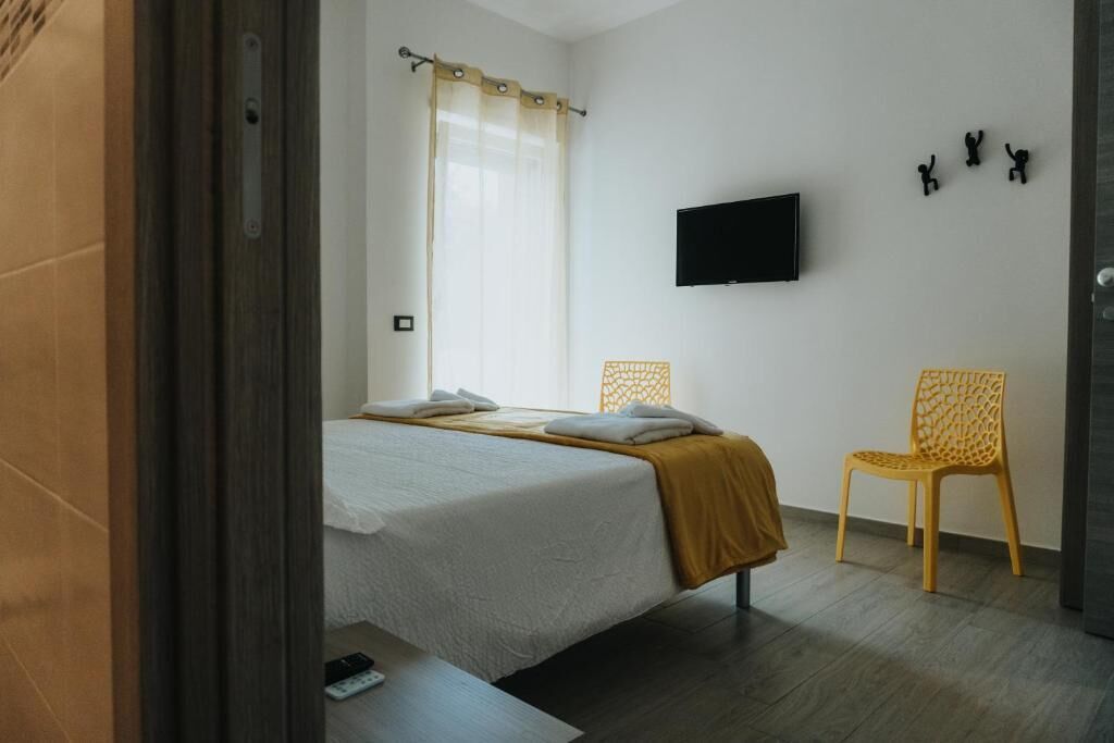 A bedroom with a bed, a chair, a TV, and a wall-mounted artwork.