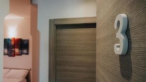 A room with a wooden door, a number '3' sign, and a bed with a white headboard. - Harmony B&B (Leporano)