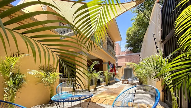 Un patio con mesas al aire libre, palmeras y fachada de edificio.
