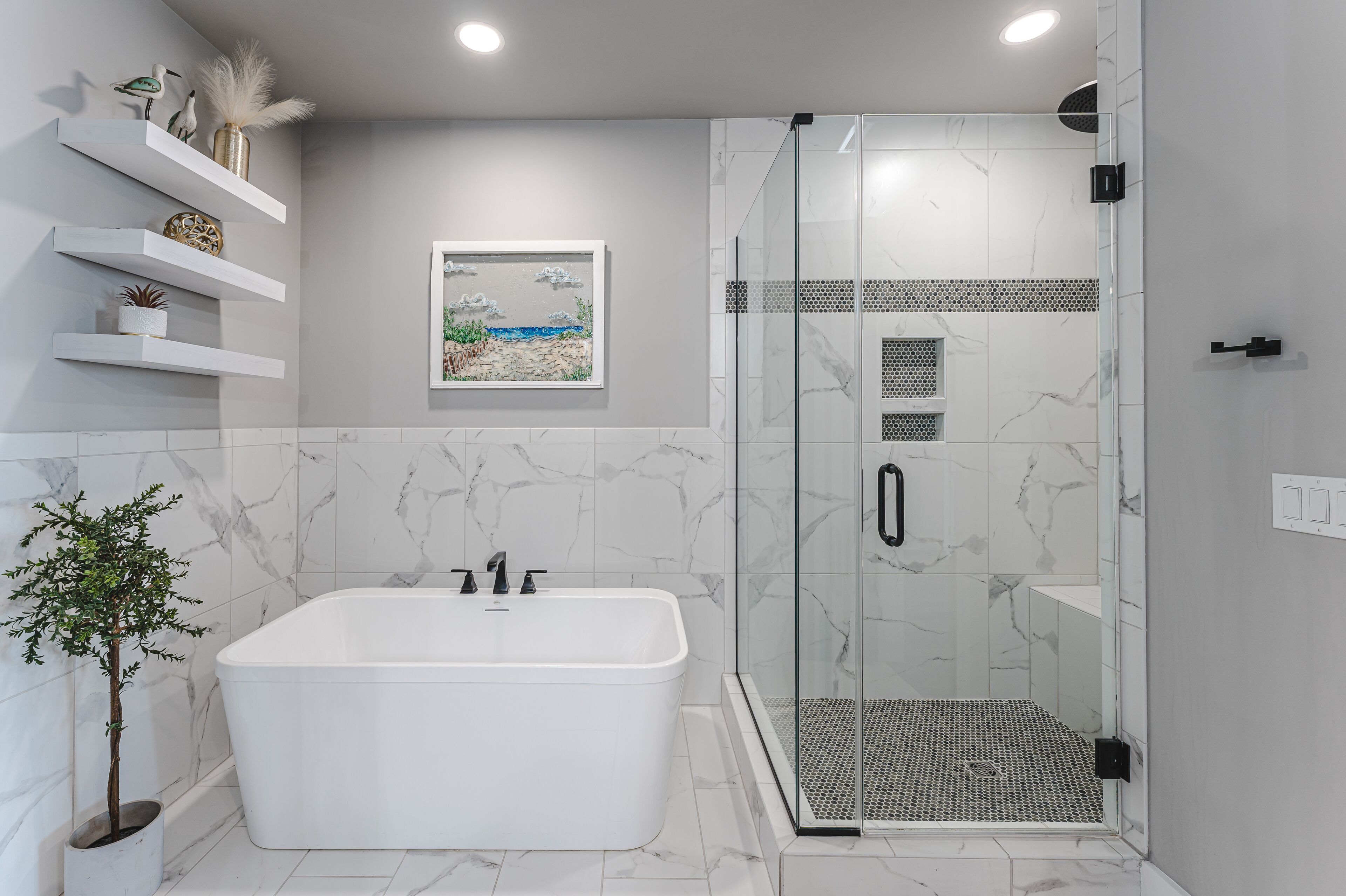 A modern bathroom with a freestanding bathtub, a glass-enclosed shower, marble walls, and a small potted plant.