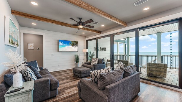 A spacious living area with a large gray sectional sofa, a small side table, and a ceiling fan. - New Windmark Phase 1 home on the beach with amazing views. (Port St. Joe)