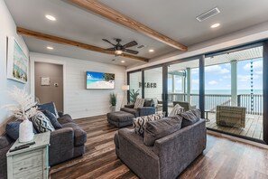 A spacious living area with a large gray sectional sofa, a small side table, and a ceiling fan. - New Windmark Phase 1 home on the beach with amazing views. (Port St. Joe)