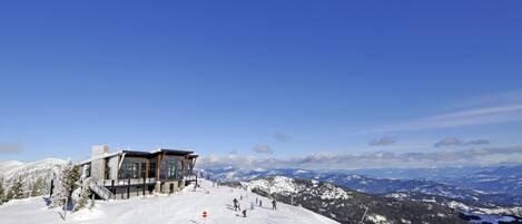 A modern ski resort with a large building, ski slopes, and snow-covered mountains.