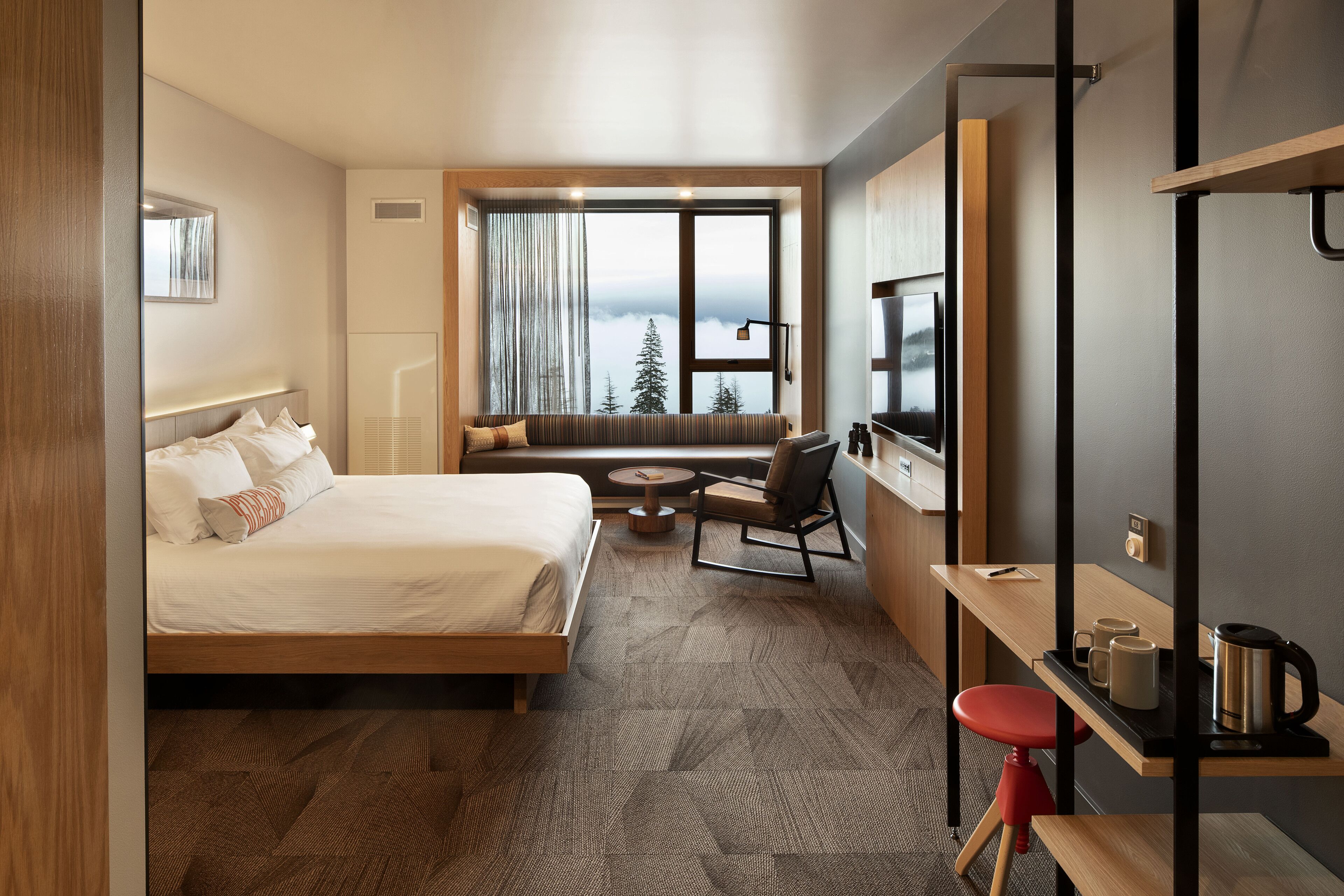 A hotel room with a bed, a seating area with a view, a desk with a coffee pot, and a TV.