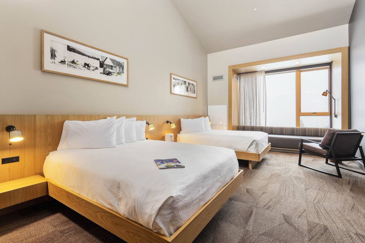 A hotel room with two beds, a sofa, a window with curtains, and wall-mounted artwork.