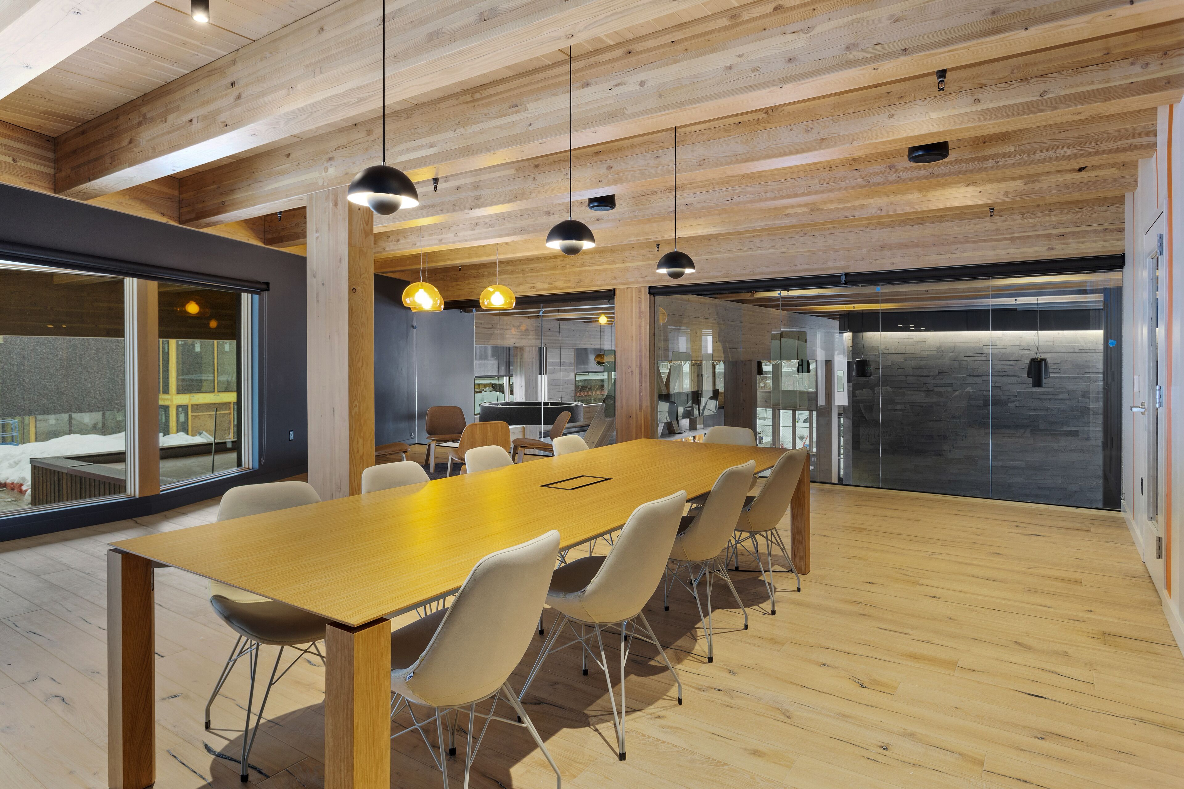 Un salón de conferencias con una larga mesa de madera, sillas blancas e iluminación colgante.