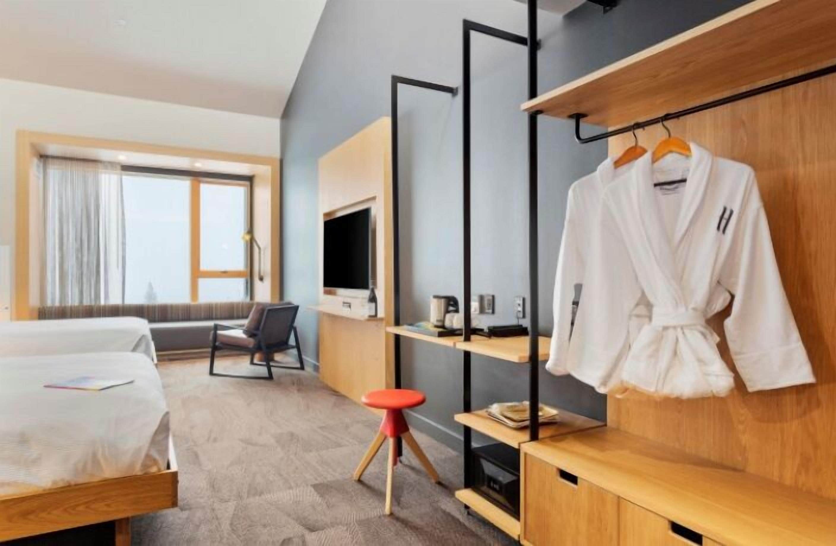 Een hotelkamer met een bed, een bureau, een televisie, een badjas en een raam met gordijnen.