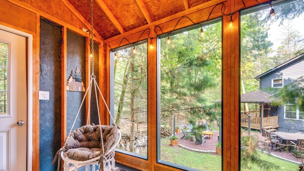 A room with large windows, a hanging chair, and a view of the outdoors. - Hot Tub, Beach Access: Albrightsville Retreat! (Albrightsville)