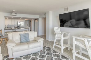 Uma sala de estar moderna com um sofá de couro branco, um tapete estampado e uma TV fixada na parede.