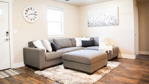A living room with a sectional sofa, ottoman, and a ceiling fan. - New family-sized home in the heart of old-town Nampa -- walking distance to NNU! (Nampa)