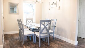 A dining area with a glass-top table, grey chairs, a chandelier, and a 'gather' sign on the wall. - New family-sized home in the heart of old-town Nampa -- walking distance to NNU! (Nampa)