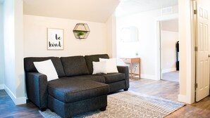 A modern living room with a sectional sofa, a decorative wall piece, and a geometric wall-mounted planter. - New family-sized home in the heart of old-town Nampa -- walking distance to NNU! (Nampa)
