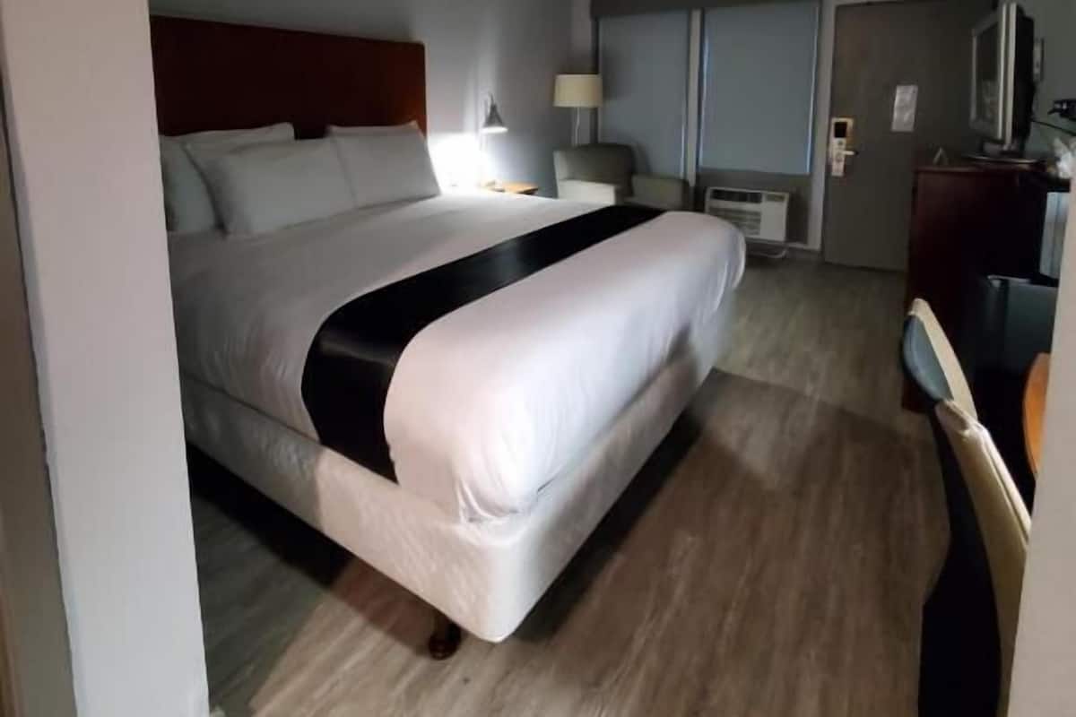 A hotel room with a large bed, bedside tables, a desk, a chair, and a television.