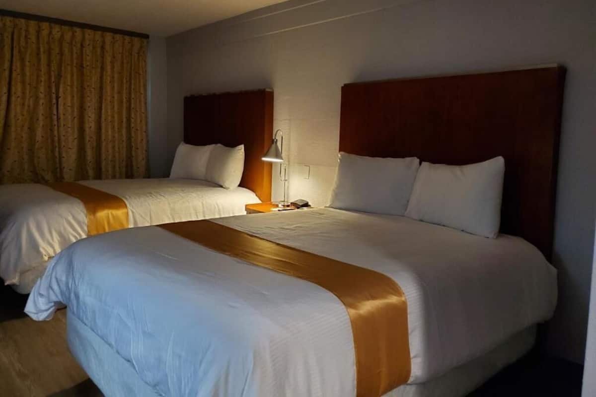 A hotel room with two beds, each with a wooden headboard, white bedding, and a brown accent.