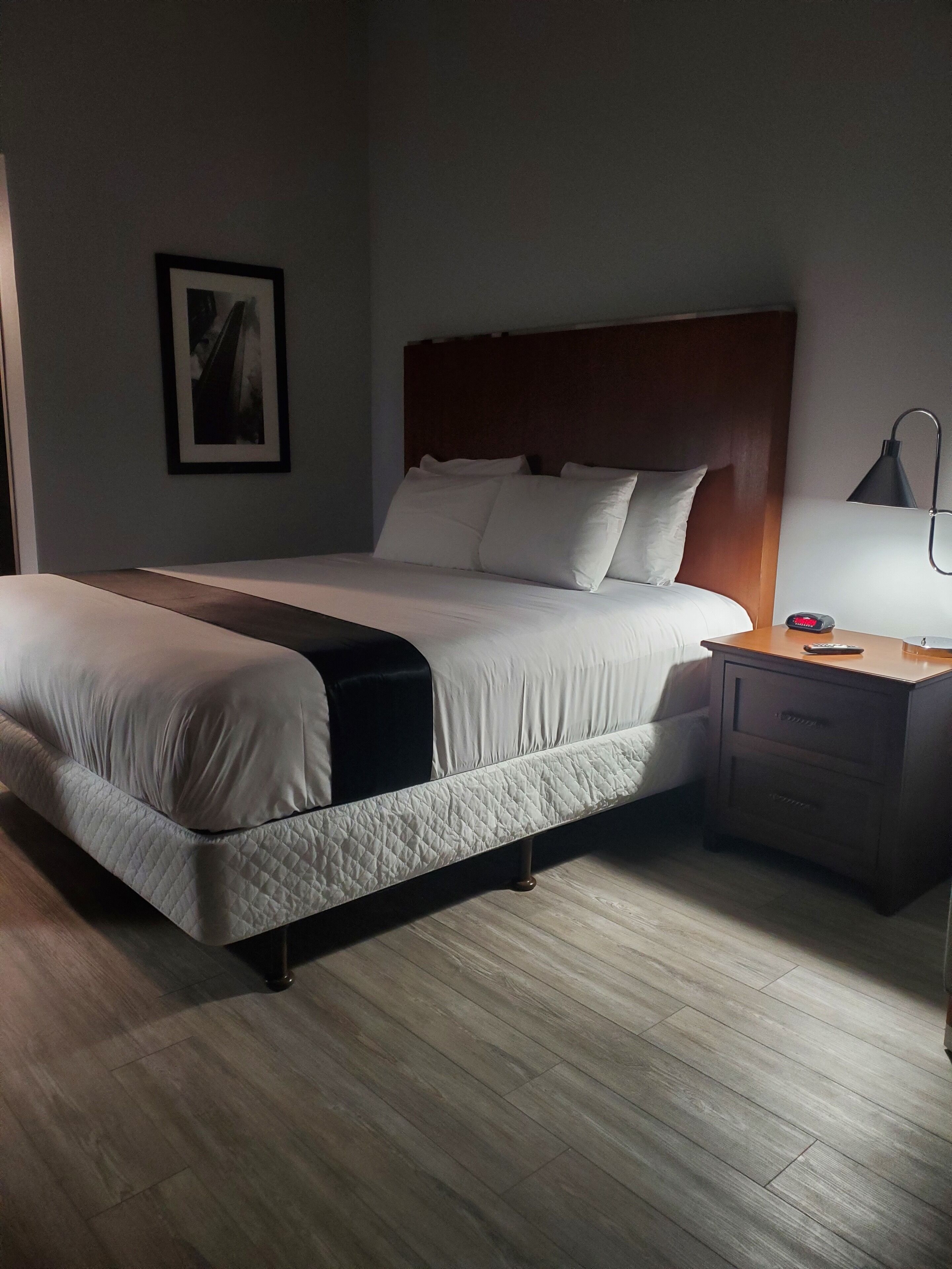 A neatly made bed with a wooden headboard, a bedside table with a lamp, and a framed picture on the wall.