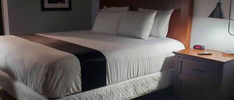 A neatly made bed with a wooden headboard, a bedside table with a lamp, and a framed picture on the wall.
