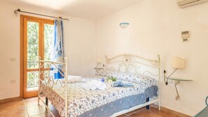 Ein Schlafzimmer mit einem Bett, einem Fenster mit Vorhang, einer Wand-Klimaanlage und einem Nachttisch mit Lampe.