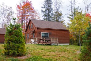 Eine Holzhütte mit einer Terrasse, umgeben von Bäumen mit Herbstlaub.