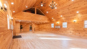 A spacious wooden interior with a high ceiling, multiple windows, and a central staircase. - Family Log Cabin Near Sauna White Mountains (Bethlehem)