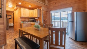 A wooden cabin interior with a kitchen, dining area, and a view through a large window. - Family Log Cabin Near Sauna White Mountains (Bethlehem)