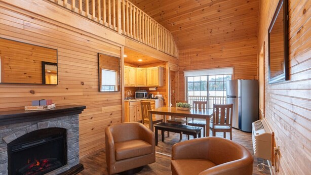 A log cabin interior with a fireplace, leather chairs, a dining table, a kitchen area, and a balcony. - Family Log Cabin Near Sauna White Mountains (Bethlehem)