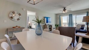 A modern dining area with a white table, blue vase centerpiece, and a ceiling fan.