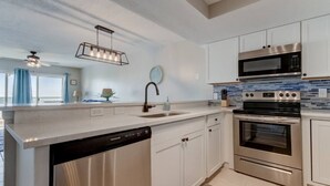 A modern kitchen with stainless steel appliances, white cabinetry, and a large island with a dishwasher.