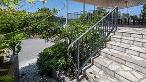 A stone staircase leading to a covered outdoor area with metal railings, surrounded by greenery and overlooking a body of water. - Panoramic Apartments Anić - Superior Two Bedroom Apartment with Terrace and Sea View (Blato)