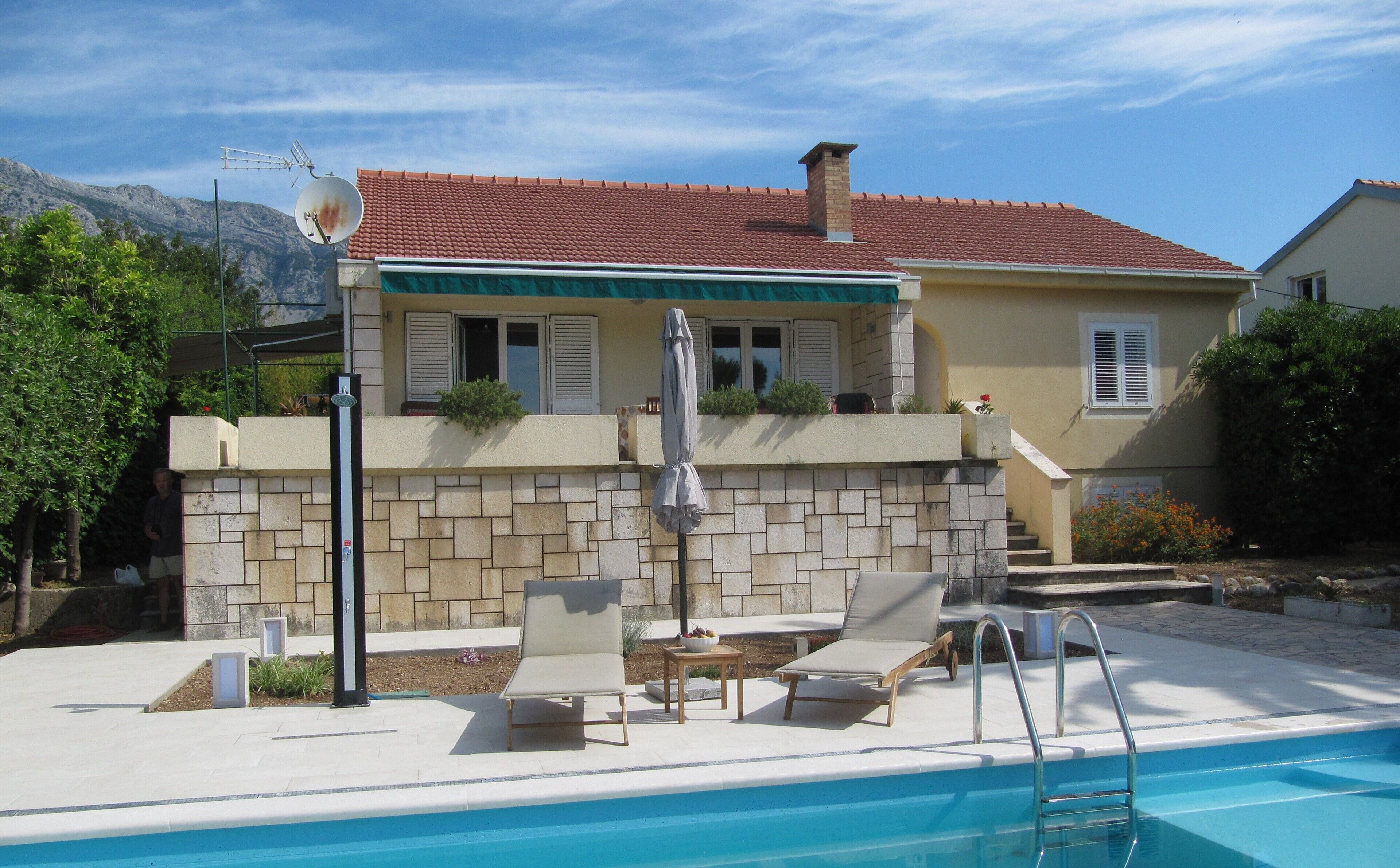 Uma casa com piscina, área de estar ao ar livre e muro de pedra.