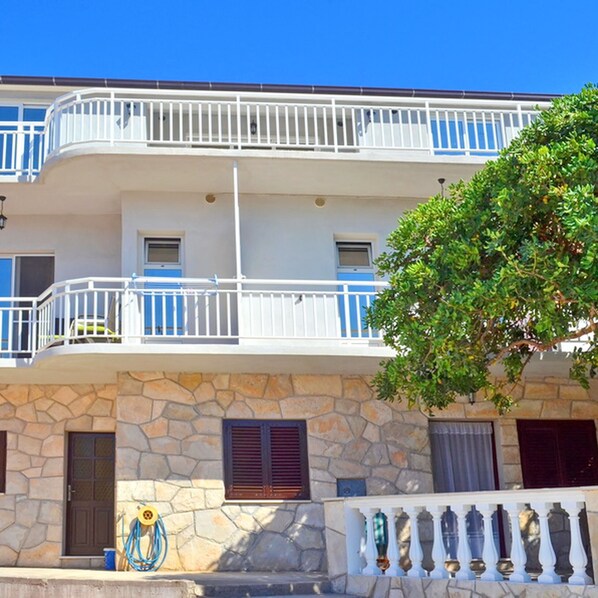 Un edificio de varios pisos con balcones, fachada de piedra y un árbol en la parte delantera.