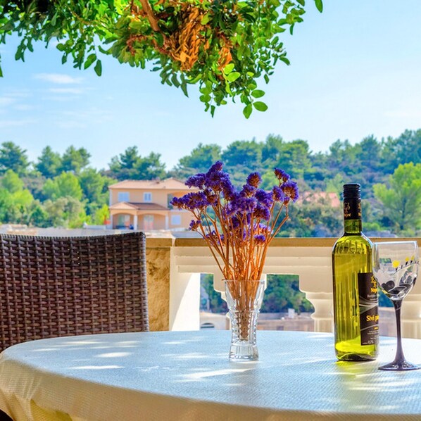 A table with a bottle and a glass, a vase with purple flowers, and a wicker chair.