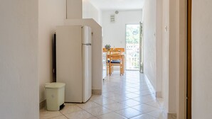 A narrow hallway with a refrigerator, a trash bin, and a dining area with a table and chairs. - Apartments Katica's Place - Two Bedroom Apartment with Terrace and Sea View (Prižba)