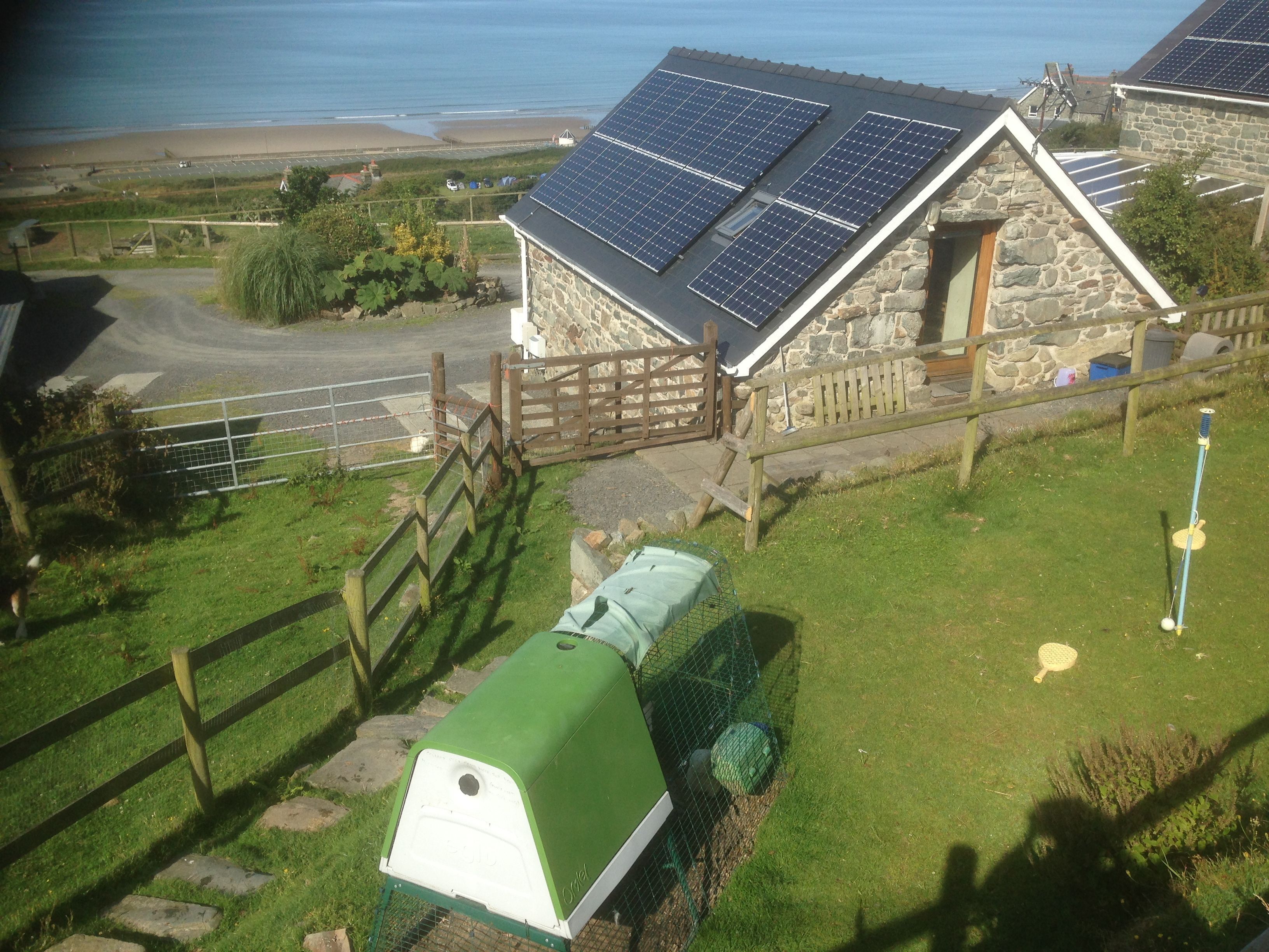 Une maison en pierre avec un toit en pente, des panneaux solaires et un abri de jardin doté d’un toit végétalisé.