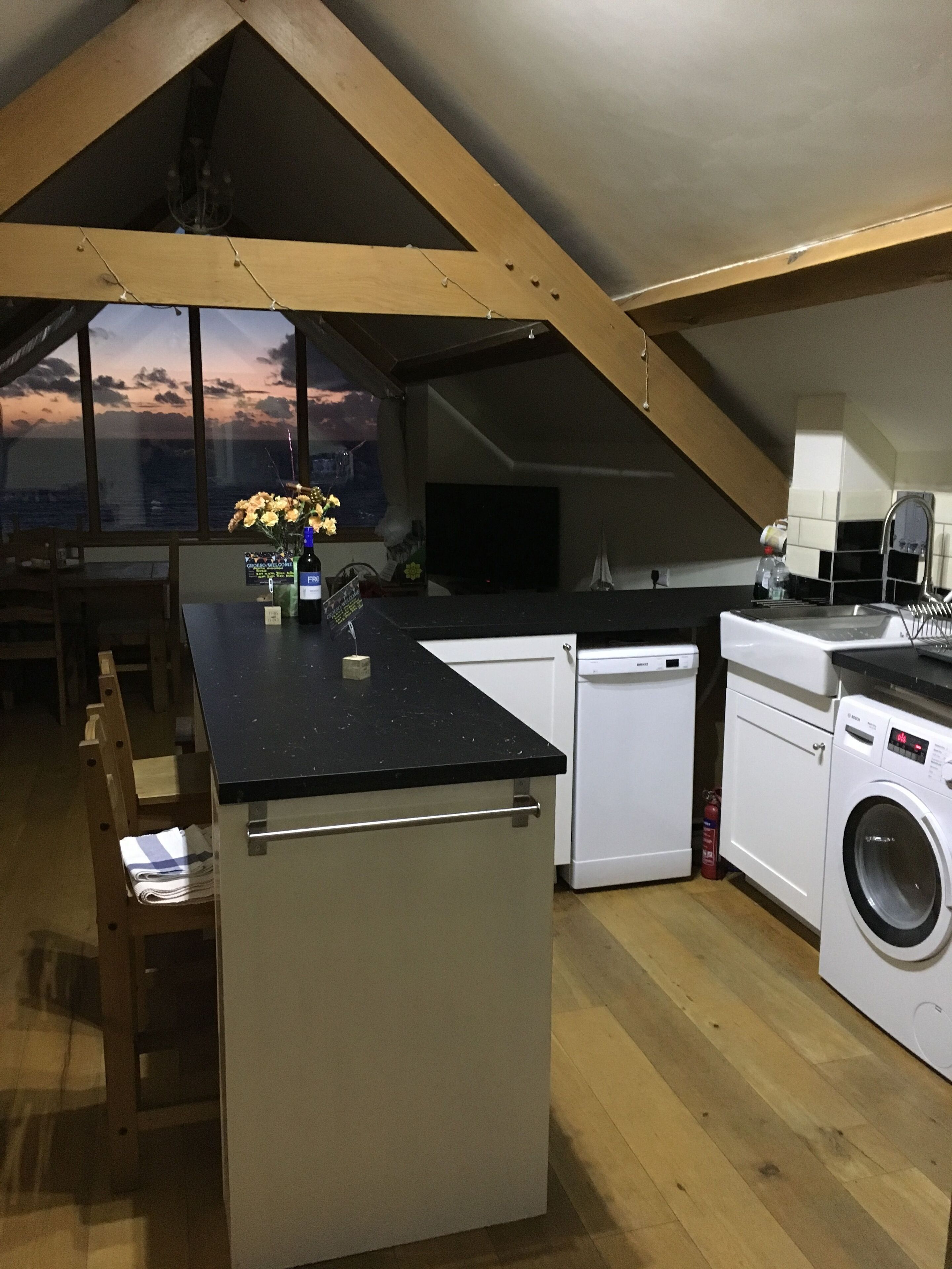 A modern kitchen with a central island, built-in appliances, and a large window offering a view of the sunset.