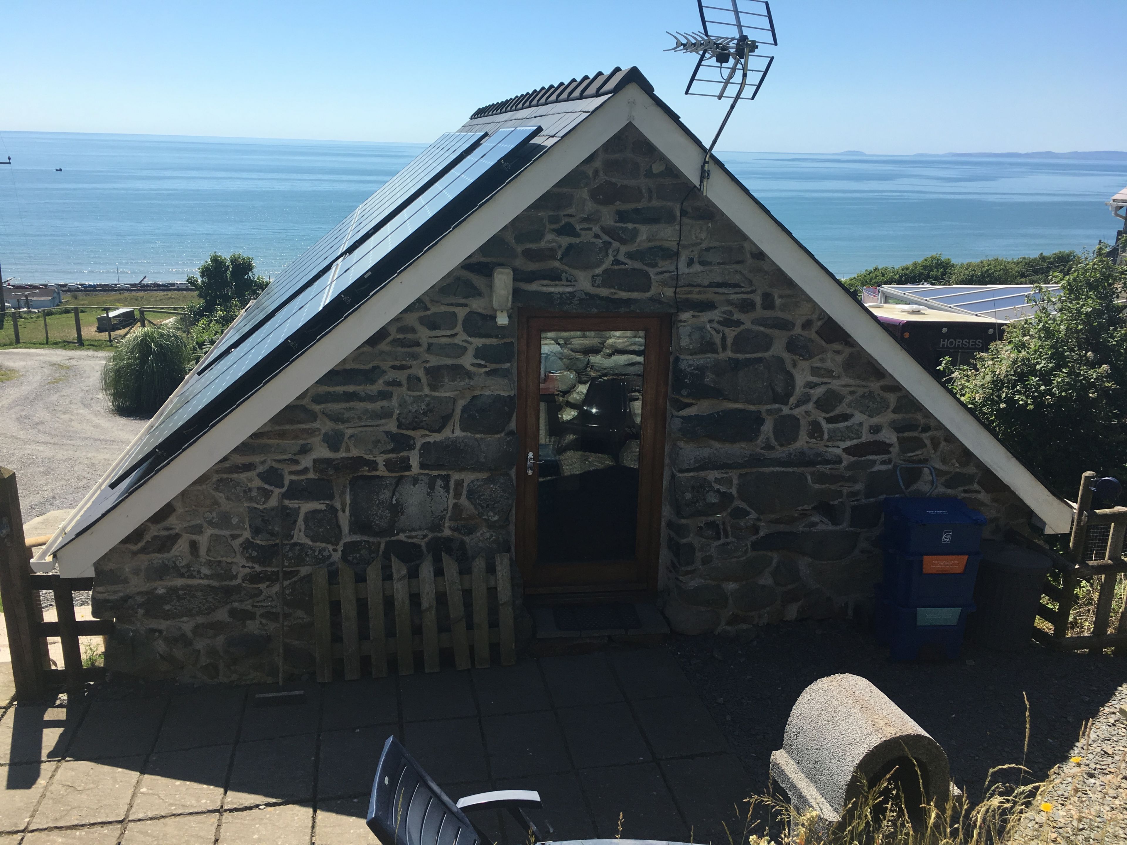A stone building with a sloped roof, a wooden door, and a view of the sea.