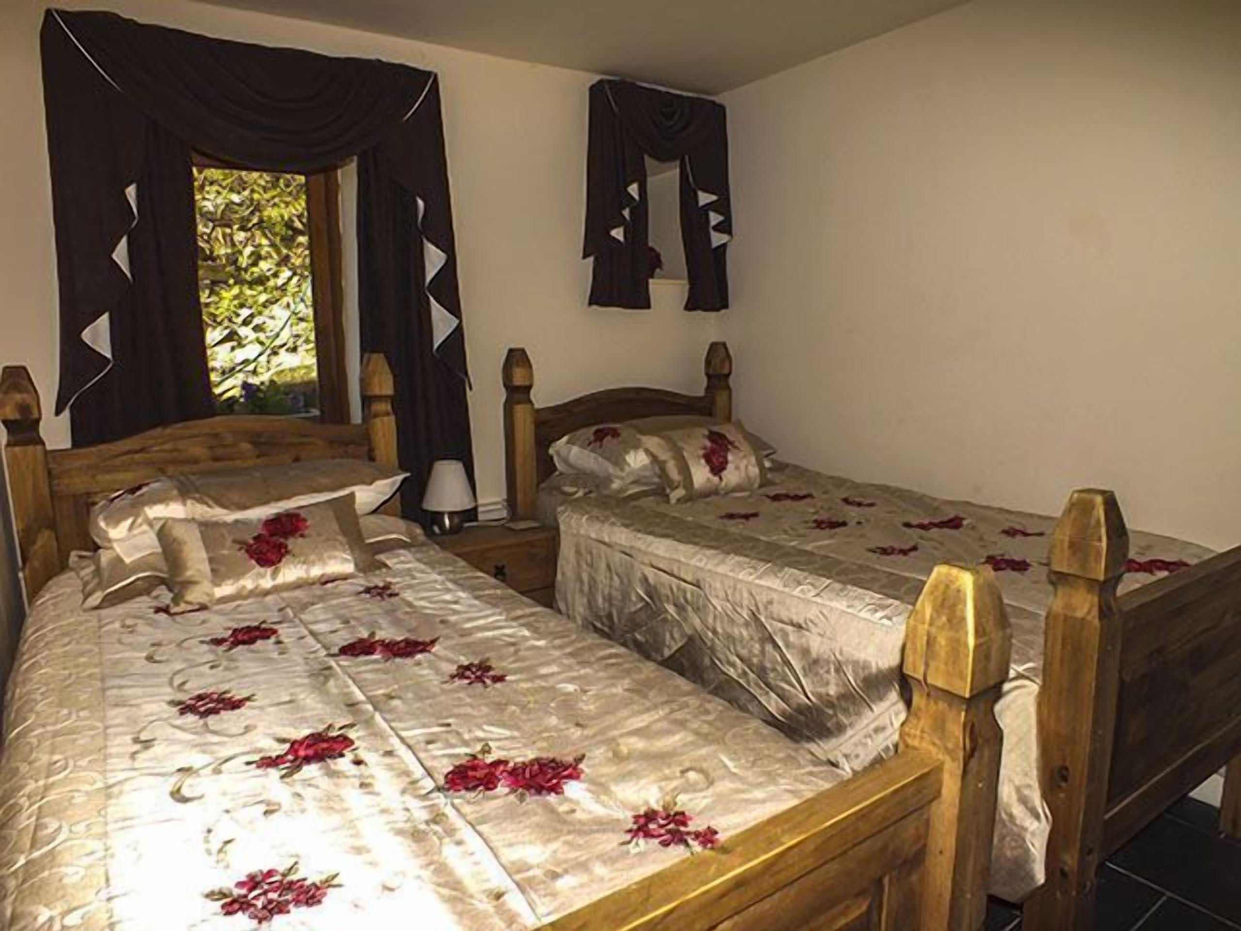 A double bed with floral bedding, a nightstand with a lamp, and a window with curtains.