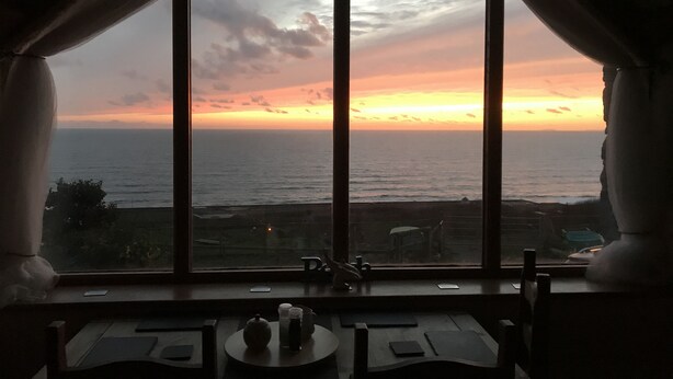 Ein Zimmer mit großem Fenster mit Blick auf den Ozean bei Sonnenuntergang.