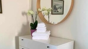 Een witte ladekast met drie lades, een ronde spiegel met houten lijst, een kleine plant in een pot en een stapel opgevouwen handdoeken.