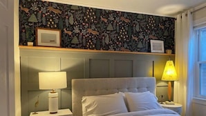 Een slaapkamer met een bed, twee nachtkastjes, een lamp en een muur met behangpapier met een natuurthema.