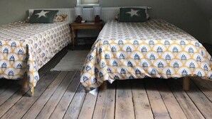 A small, cozy attic bedroom with two single beds, a wooden floor, a window, and a small table.