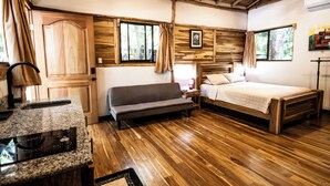A wooden-floored room with a sofa, a bed, a small table, and a window with curtains. - RusTeak Living Boutique Hotel Mango Studio - a Refuge in Nature (Provincia de Guanacaste)