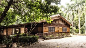 A rustic wooden cabin with a porch, surrounded by lush greenery and palm trees. - RusTeak Living Boutique Hotel Mango Studio - a Refuge in Nature (Provincia de Guanacaste)