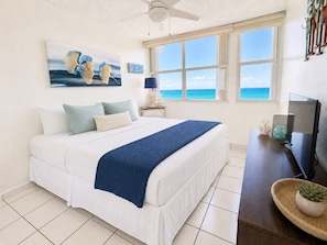 A bedroom with a bed, a television, a window with a view of the ocean, and a ceiling fan. - Beachfront Gem * Walk 2 Eat *W/D (Carolina)