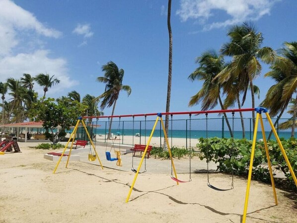 A beach with a swing set, palm trees, and a clear view of the ocean.