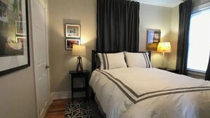 A hotel room with a large bed, a nightstand with a lamp, a framed picture on the wall, and a window with curtains.