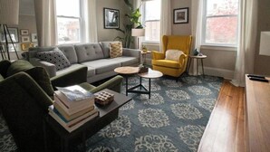 A living room with a sofa, armchair, coffee table, and a patterned carpet.