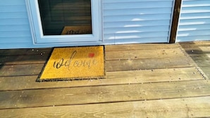 Eine Haustür mit Glasfenster, ein hölzernes Willkommensschild, ein Laternenlicht und eine Fußmatte mit dem Schriftzug 'welcome'.