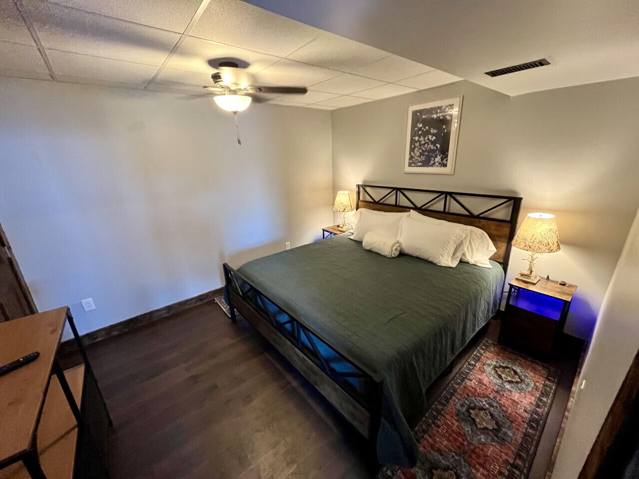 Une chambre à coucher avec un lit, deux tables de chevet, un ventilateur de plafond et un tapis.